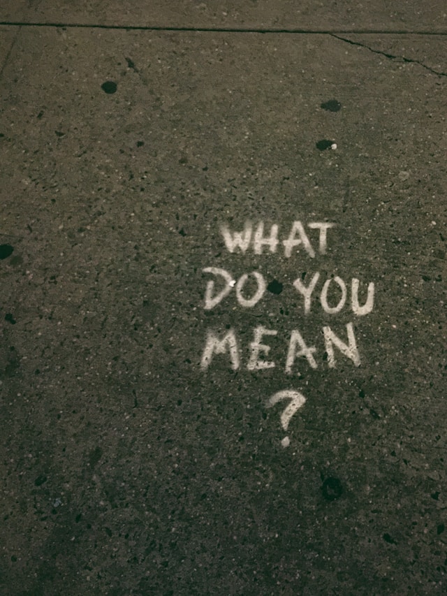 The phrase “What do you mean?” written in white on concrete. 