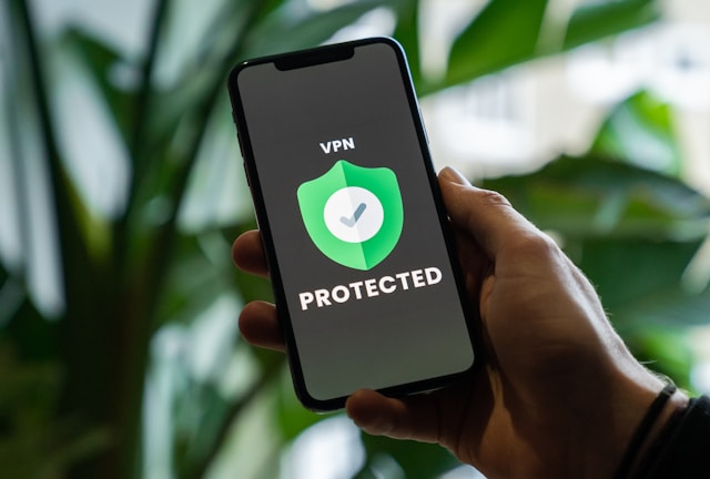 privecstasy-CXlqHmQy3MY-unsplash - GeoPlugin - Resources Someone holding a mobile phone that is displaying on its screen the words “VPN protected.”